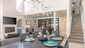 Un espace de restauration moderne avec une longue table dressée pour un repas, une cuisine en arrière-plan et un escalier.