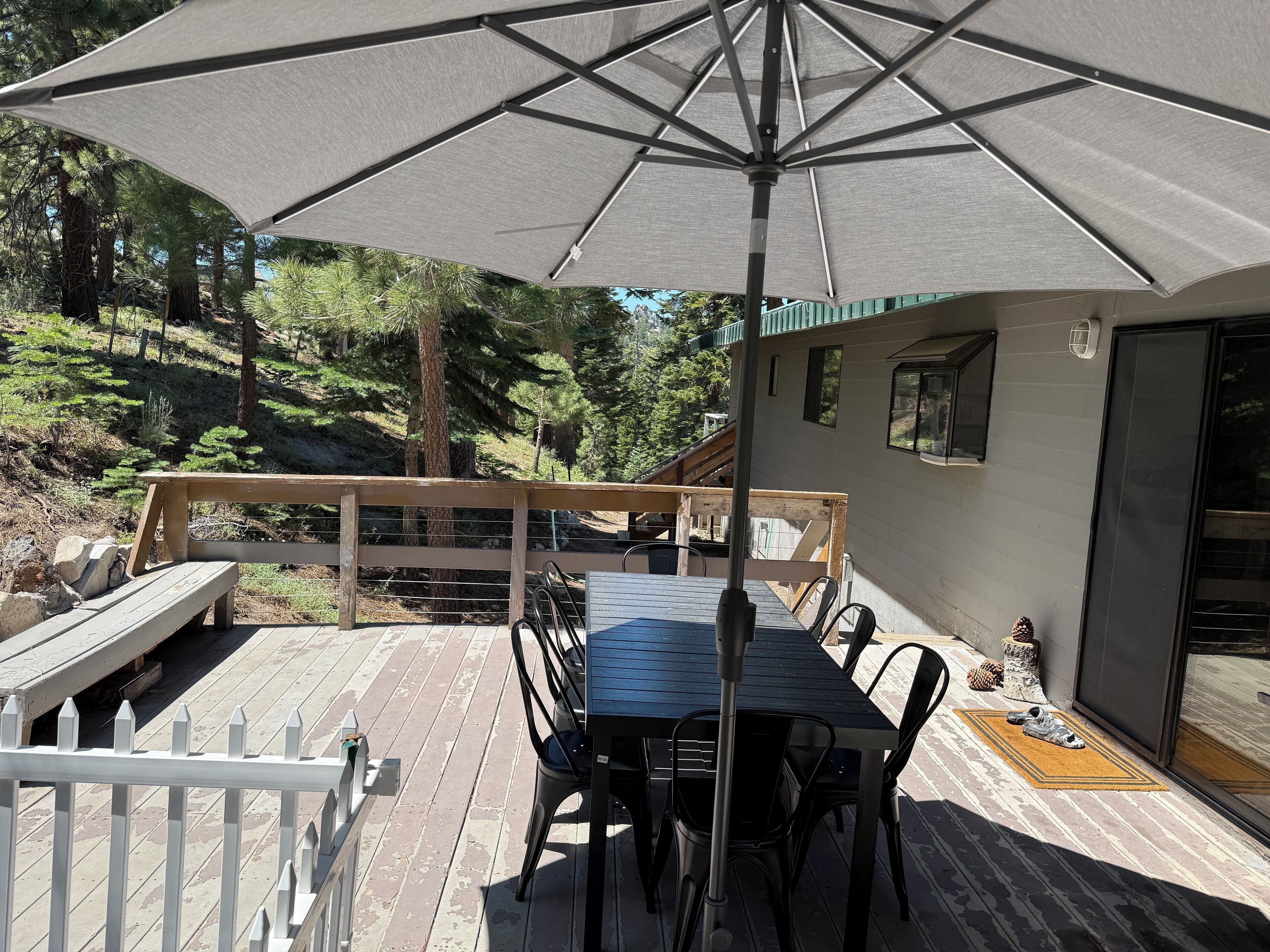 Une terrasse en bois avec une table et des chaises, protégée par un grand parasol, et offrant une vue sur une colline boisée.