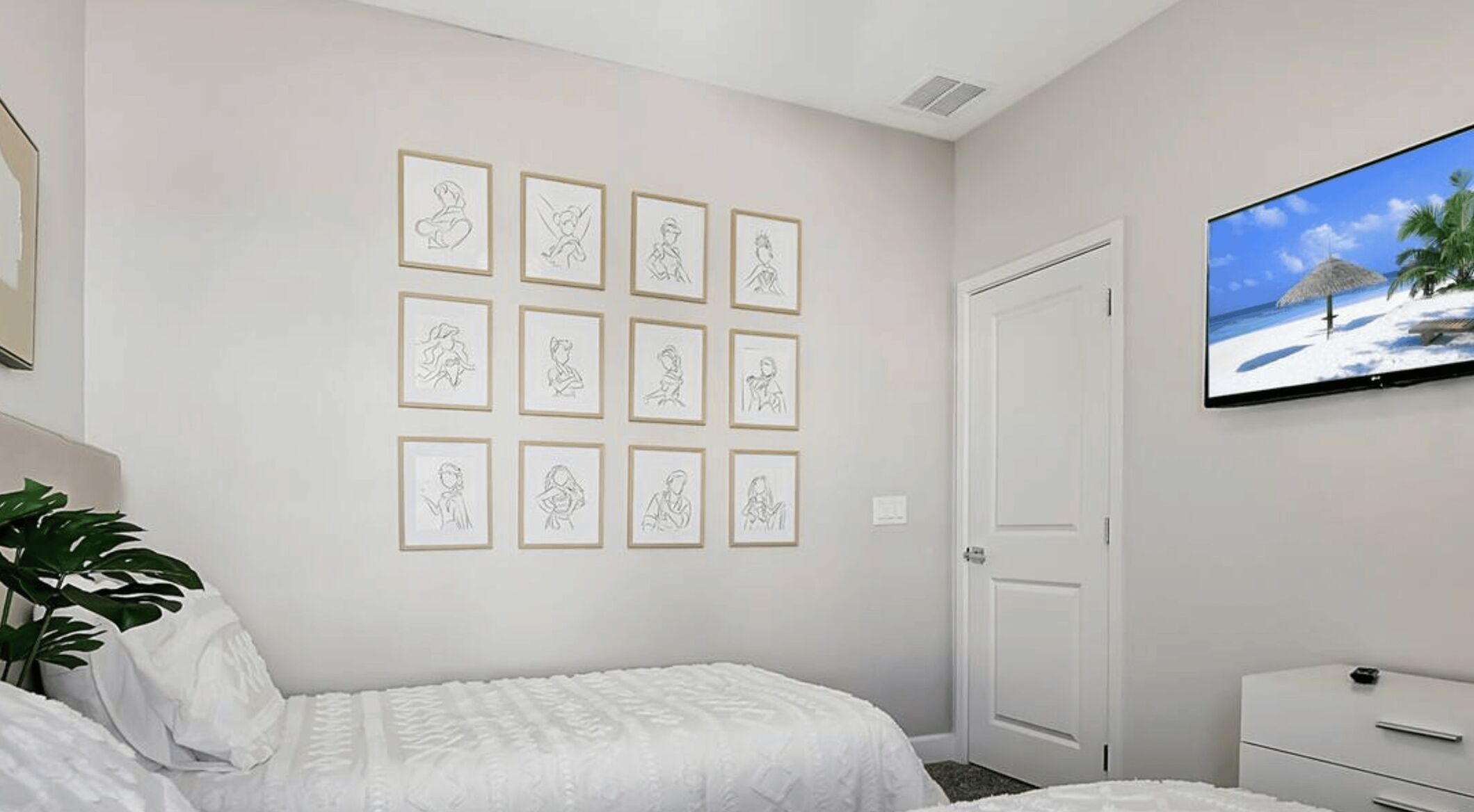 Un dormitorio con cama, televisor montado en la pared y cuadros enmarcados.