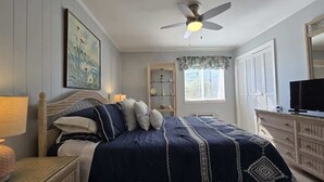 Une chambre à coucher avec un lit, un ventilateur de plafond, une commode et un téléviseur.