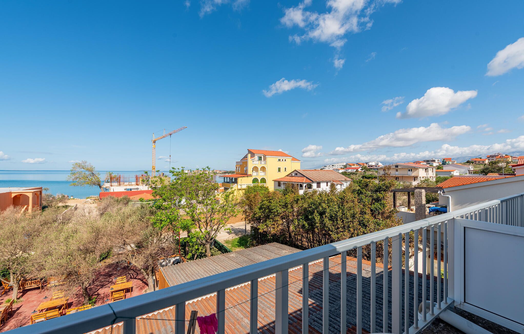 Zona residencial con vista al mar, una grúa y un edificio amarillo con tejado rojo.