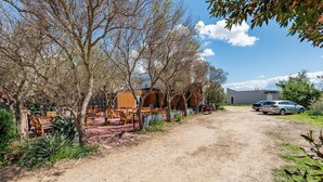 A rustic outdoor seating area with wooden furniture and a dirt path leading to a building.