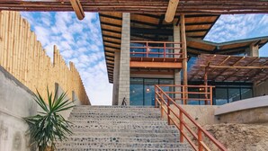 Una escalera conduce a la entrada de un edificio con estructura de techo de madera y una planta en maceta al pie.