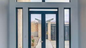 Un interior moderno con techo alto, ventanas amplias y una puerta central que da a un espacio exterior.