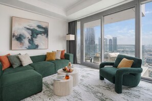 Een moderne woonkamer met een groene bank, een ronde salontafel en een stadsgezicht door grote ramen.