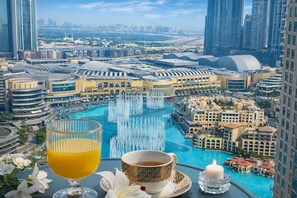 Un hotel moderno con vistas a un paisaje urbano, una piscina con fuentes y una mesa con una bebida y una vela.