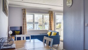 A modern living room with a dining table, blue sofa, and a large window. - 2 bedroom accommodation in Lowestoft (Lowestoft)