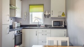 A compact kitchen with a microwave, stove, sink, and a window with a green blind. - 2 bedroom accommodation in Lowestoft (Lowestoft)
