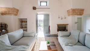 Un salón amplio con dos sofás grises claros, una mesa de centro de madera con una planta, una chimenea y un tragaluz pequeño.