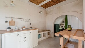 Cuina amb armaris blancs, tauleig de fusta i una prestatgeria penjant per a gots i olles.