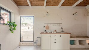 Una cuina moderna amb armaris blancs, tauleig de fusta i finestra amb vista a un pati.