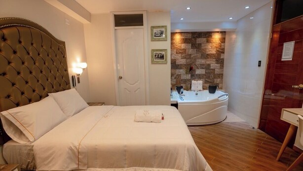 Habitación de hotel con una cama grande, un baño con bañera y una mesita.
