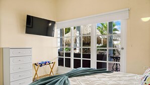 Une chambre à coucher comprenant un lit, un téléviseur fixé au mur, une armoire et un balcon avec vue sur les palmiers.