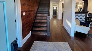 A wooden staircase with a chandelier, a patterned rug, and a kitchen area in the background. - Charming, Fully Restored 1.5 Story Farmhouse on Acreage (Muenster)