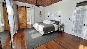 A bedroom with a wooden ceiling, a bed with grey bedding, a nightstand, and a door with frosted glass panels. - Charming, Fully Restored 1.5 Story Farmhouse on Acreage (Muenster)