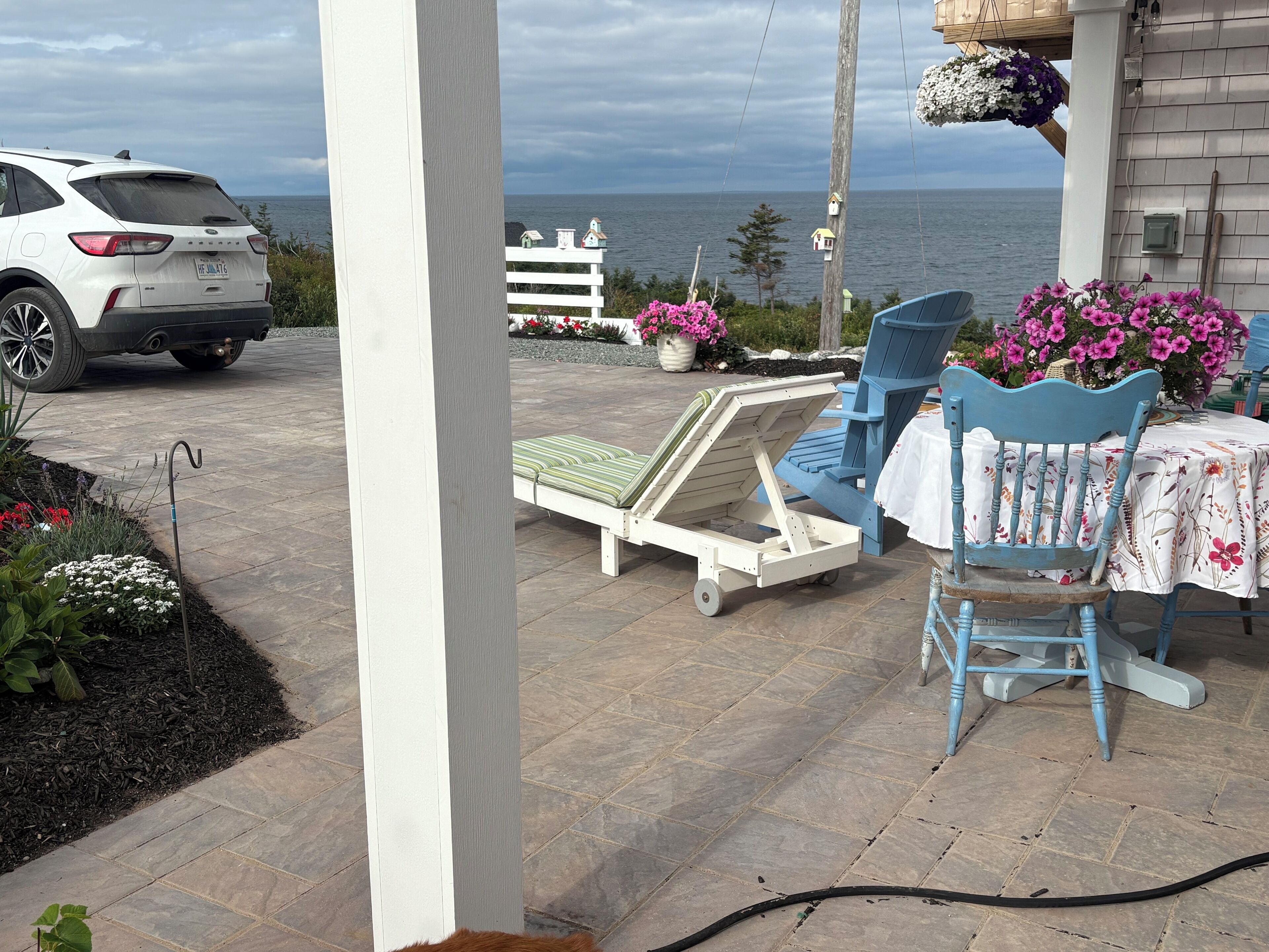 A patio with a white car parked, a small table with a white tablecloth, and a blue chair.