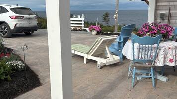 A patio with a white car parked, a small table with a white tablecloth, and a blue chair.