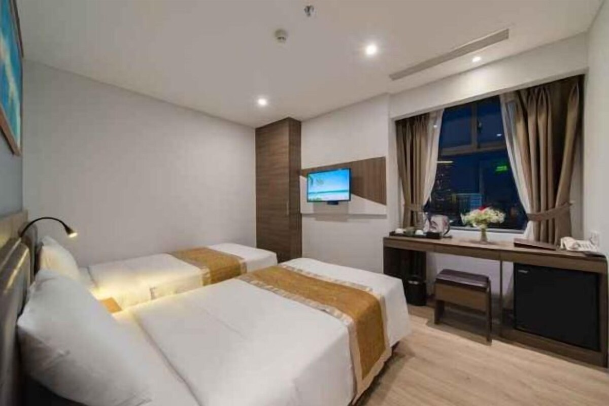 A hotel room with two beds, a desk, a TV, and a window with curtains.