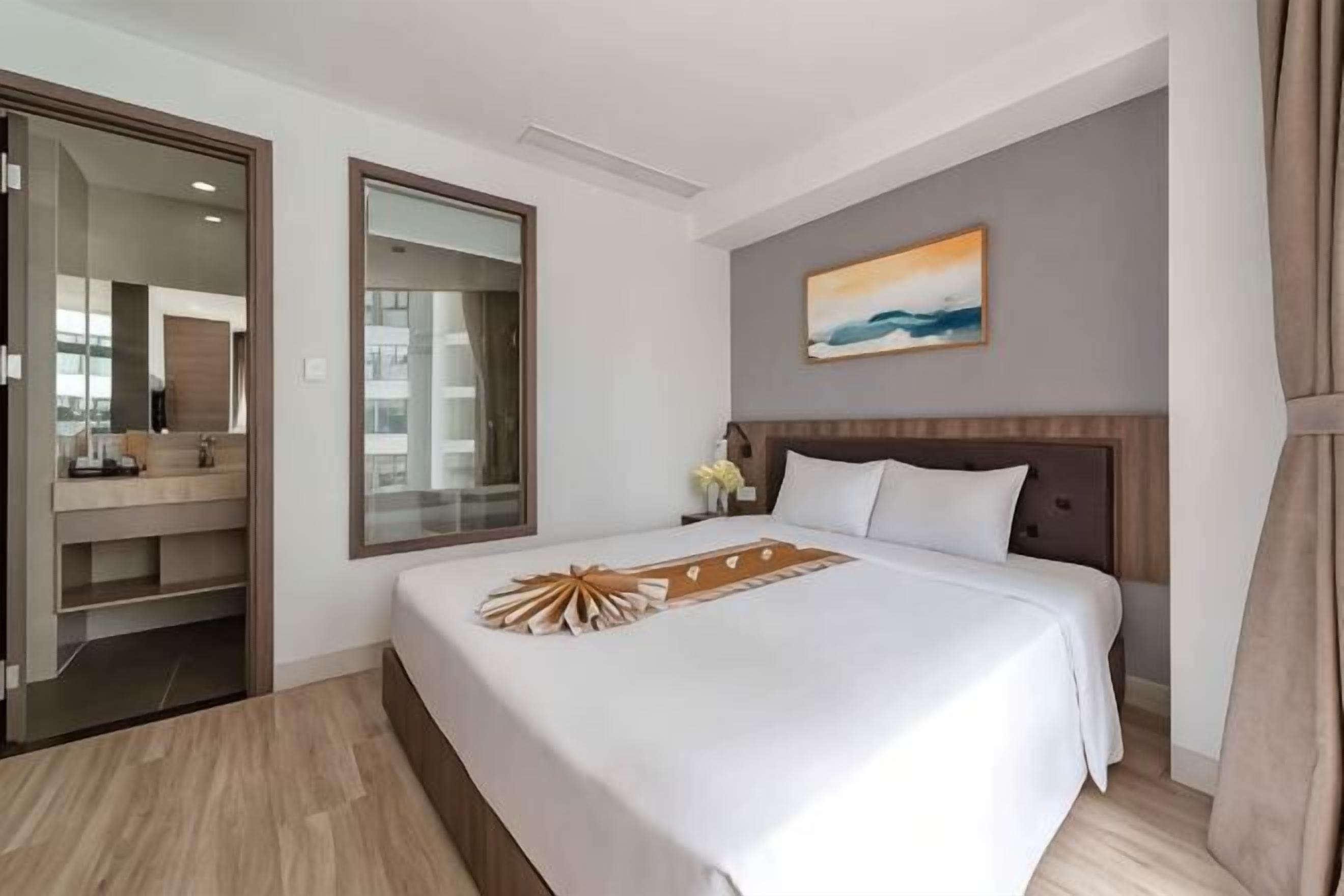 Quarto de hotel com cama, um espelho grande, um quadro e chão de madeira.