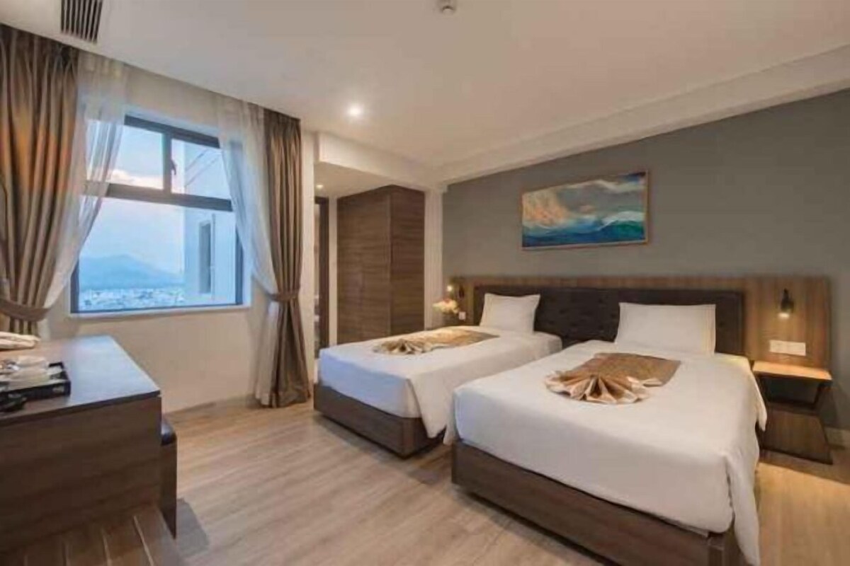 A hotel room with two beds, a desk, and a view of the city.