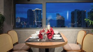 A dining table set for two with a city view through large windows. - Zenia Boutique Hotel Nha Trang (Nha Trang)