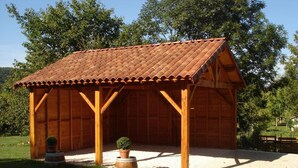 A wooden pavilion with a tiled roof, surrounded by gravel and grass, with trees in the background.