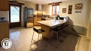 A modern kitchen with a central island, bar stools, a refrigerator, and a window with curtains.
