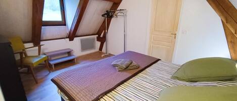 A bedroom with a bed, a chair, a desk, a radiator, and a window.