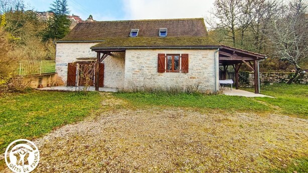 A stone house with a sloped roof, wooden shutters, and a covered porch.
