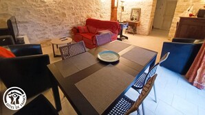 A cozy living room with a stone wall, a red sofa, a dining table with chairs, and a small round table with a lamp.