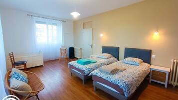 Une chambre avec deux lits, une chaise, un bureau et un radiateur.