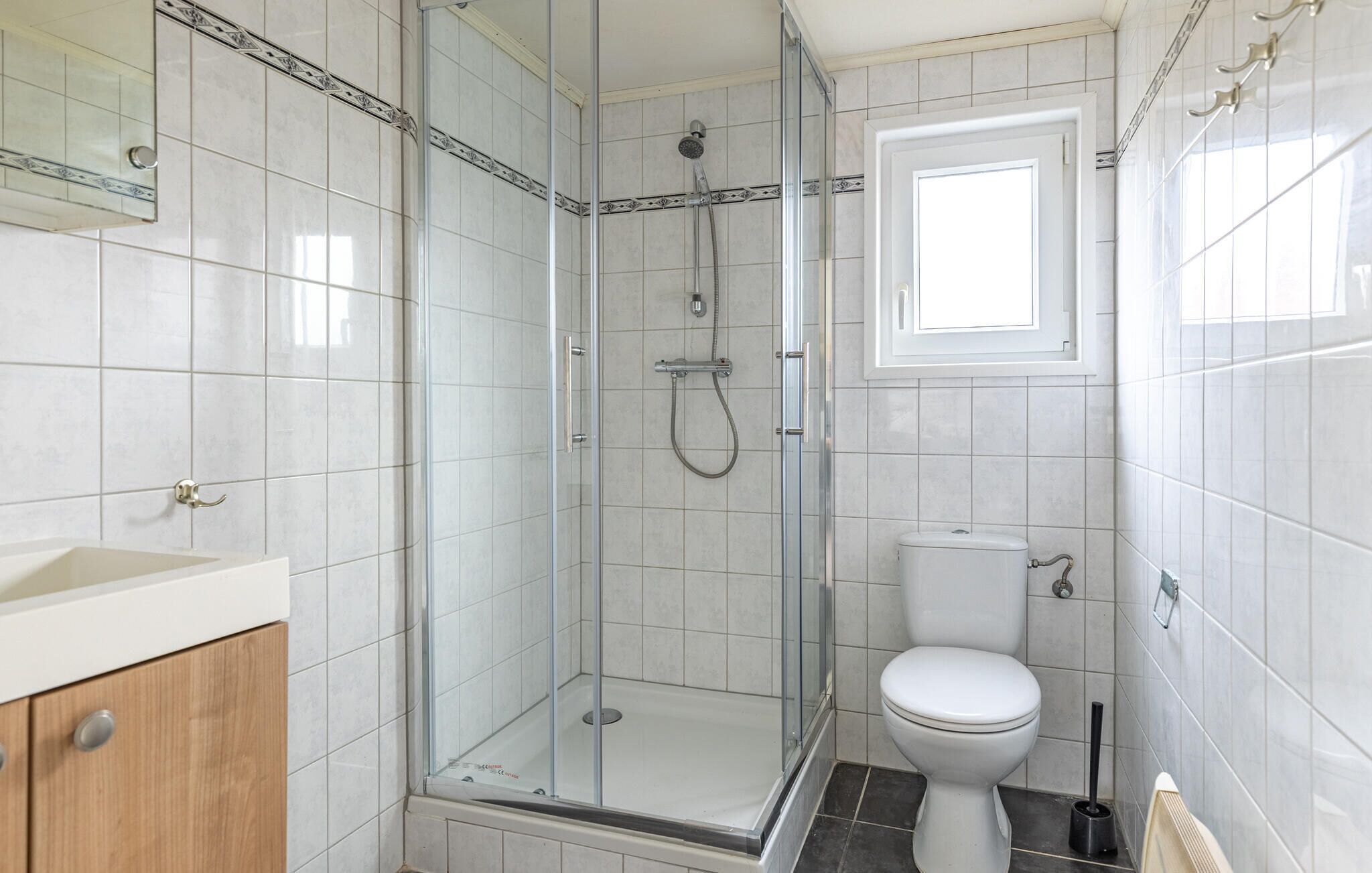 Un baño con ducha de vidrio, inodoro y lavabo con gabinete de madera.