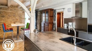 Una cocina con pared de piedra, armarios de madera, extractor de acero inoxidable y una zona de bar con taburetes.