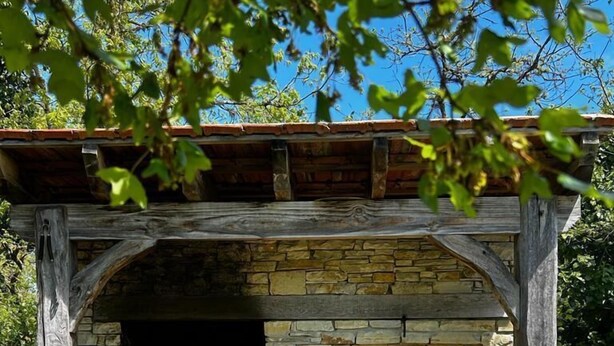 Cocina exterior de piedra con horno de ladrillo y zona de parrillada, rodeada por una pérgola de madera.