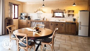 Una cocina con armarios de madera, una mesa redonda con sillas, una estufa, un microondas y un refrigerador.