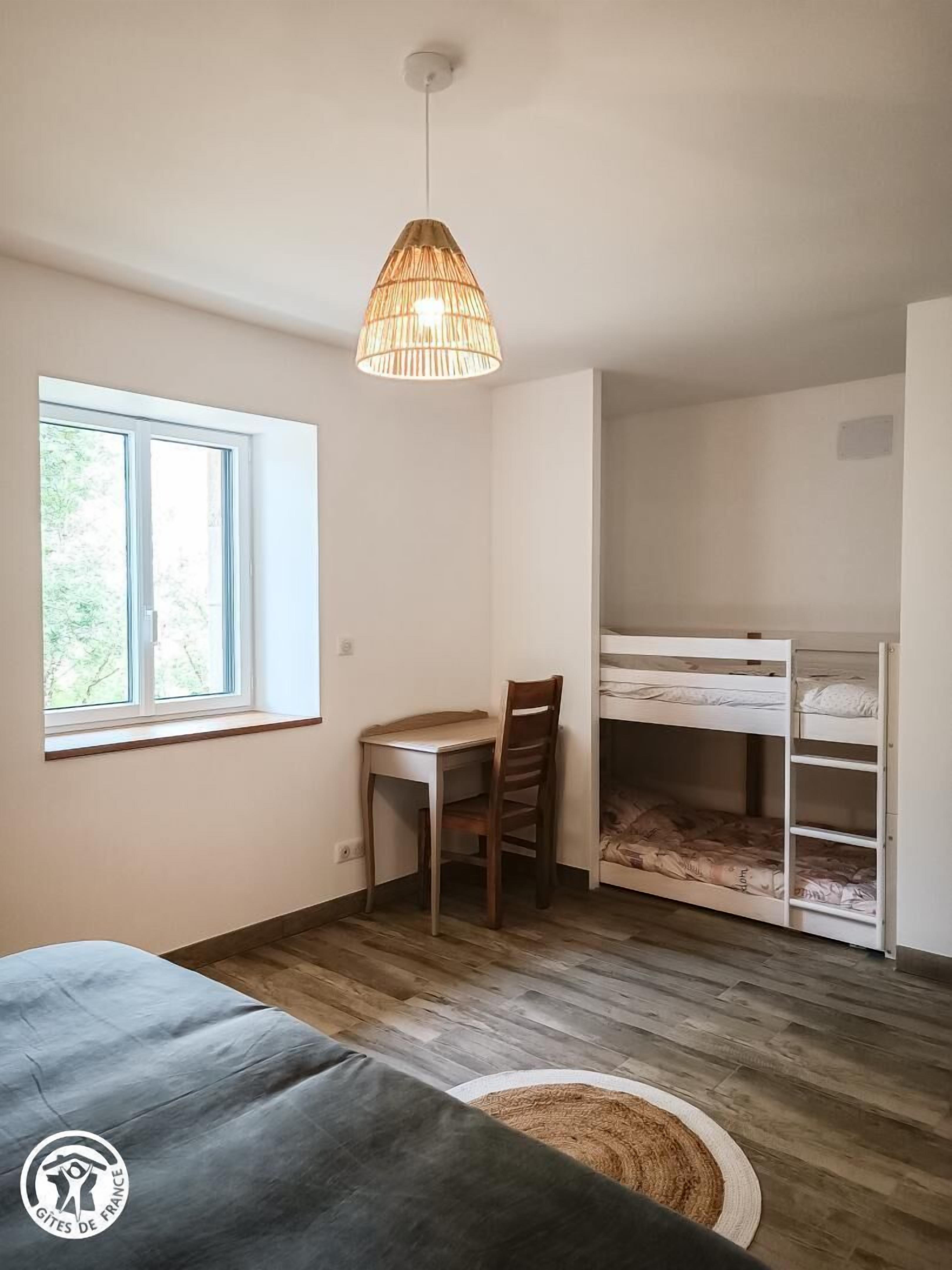 Una habitación con literas, un escritorio, una silla, una lámpara colgante y una ventana.