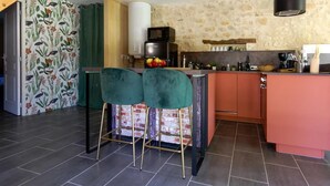 Cocina con isla central, taburetes verdes, microondas y pared de piedra.