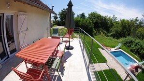 Un balcón con una mesa y sillas de metal rojo, una piscina y un césped verde.