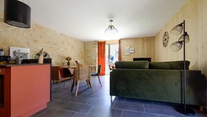 Una sala de estar acogedora con un sofá verde, una mesa de comedor con sillas, y una zona de cocina con encimera y electrodomésticos.