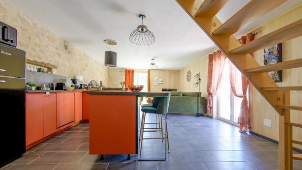 Una cocina moderna con una isla central, un comedor con un sofá verde y una escalera de madera.