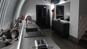 A modern kitchen with a long countertop, a sink, and a stove. There is a door leading to another room and a mirror above the counter. - Gîtes de France® - VIP REFUGE (LE VIGNON-EN-QUERCY)