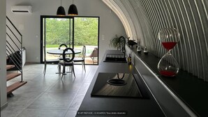 A modern kitchen with a curved ceiling, a dining area with a table and chairs, and a view of the outdoors. - Gîtes de France® - VIP REFUGE (LE VIGNON-EN-QUERCY)