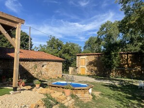 A stone house with a tiled roof, a wooden pergola, and a swimming pool.