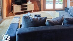 A cozy wooden cabin interior with a sofa, TV, and shelves. - Gîtes de France® - The Chalet (PINSAC)