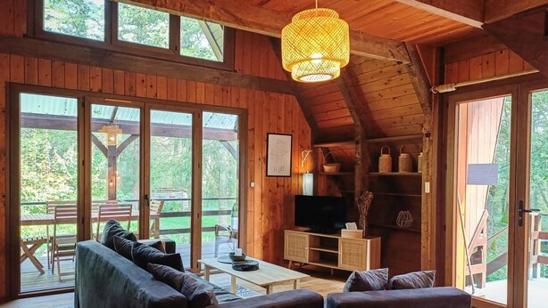 A cozy cabin interior with a sofa, TV, and wooden shelves. - Gîtes de France® - The Chalet (PINSAC)