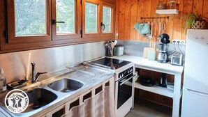A compact kitchen with wooden walls, a sink, a stove, and a countertop with various appliances. - Gîtes de France® - The Chalet (PINSAC)