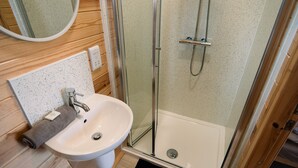 A bathroom with a glass-enclosed shower, a white sink, and a wooden floor. - Cosy En-suite Cabin in Moray Speyside (Kinloss)
