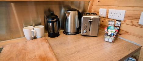 Une petite cuisine équipée d’une bouilloire en acier inoxydable, d’un grille-pain, de deux tasses blanches et d’un carton de lait.