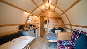 A compact, wooden interior with a dining area, kitchenette, and a sleeping area with a sofa and a bed. - Cosy En-suite Cabin in Moray Speyside (Kinloss)