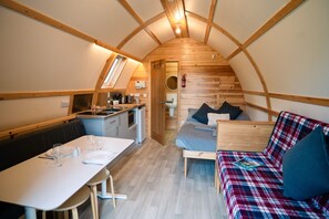 A compact, wooden interior with a dining area, kitchenette, and a sleeping area with a sofa and a bed. - Cosy En-suite Cabin in Moray Speyside (Kinloss)